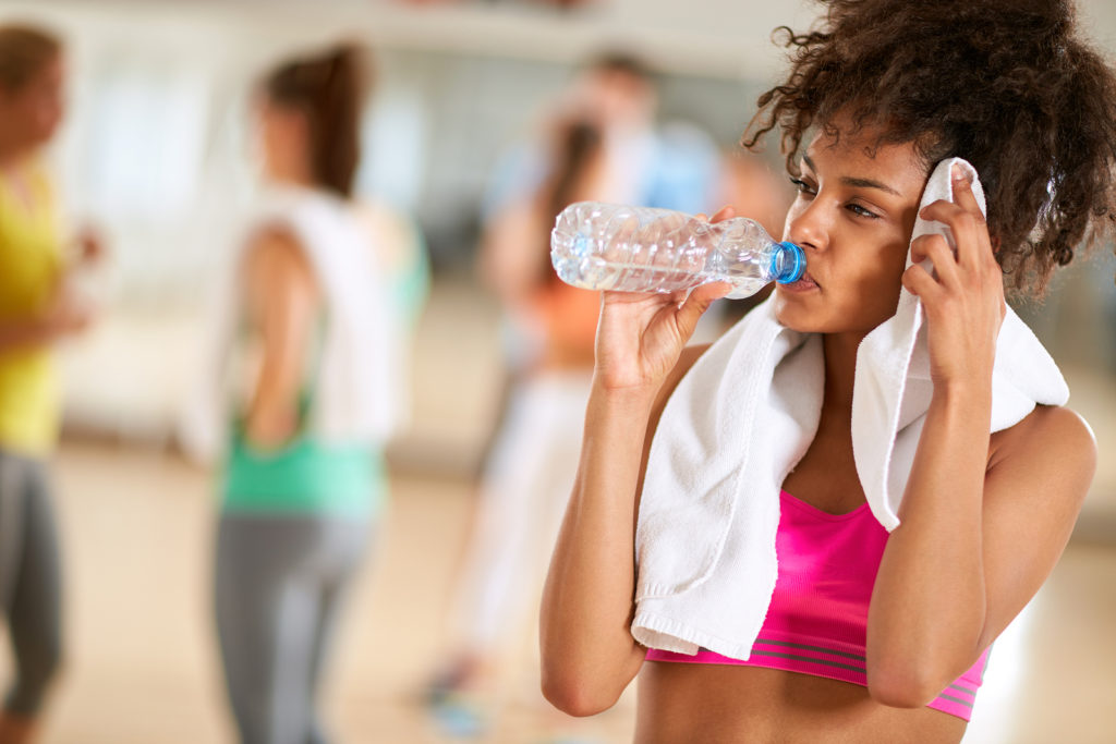 Thirsty half-caste girl after hard body training drink water and wipes sweat at gym