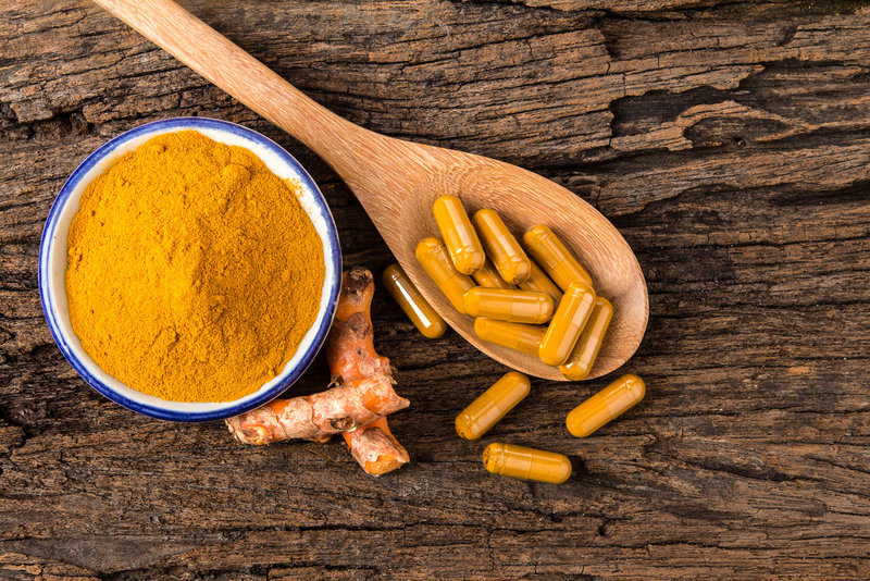 the turmeric powder capsule and roots curcumin on wooden plate