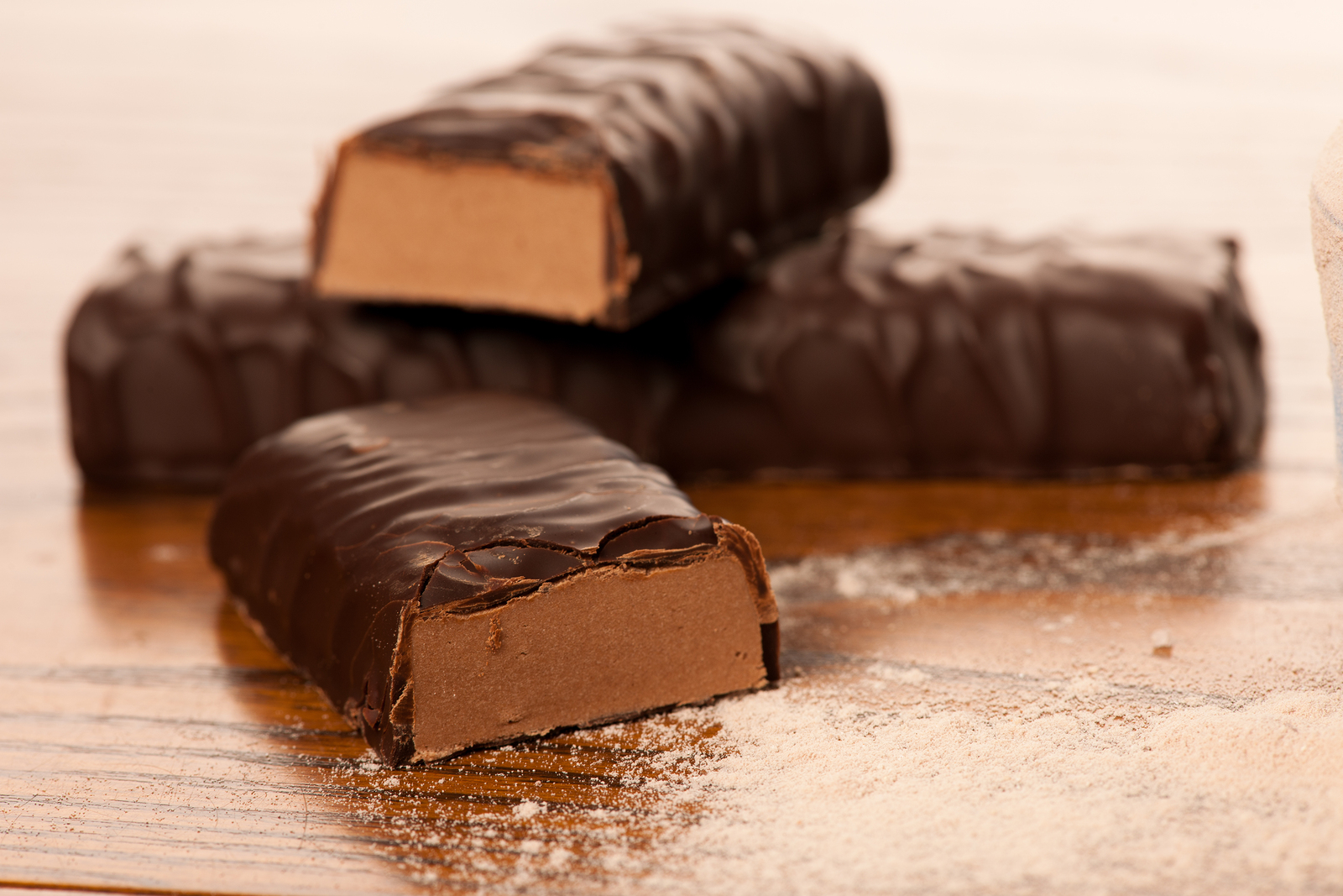 Whey protein powder and chocolate protein bar on wooden background.